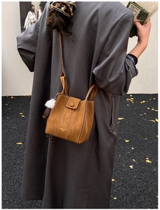 Close-up of brown suede bucket bag with gold lettering and decorative plush charm