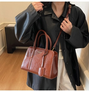 Deep brown glossy leather handbag with top handles and adjustable shoulder strap worn by model