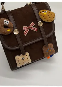 Detail of vintage brown satchel featuring plush charms and plaid bow decoration