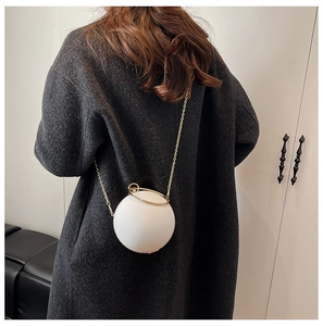 Detail of white spherical crossbody bag with gold ring handle and chain on black coat