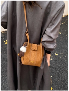 Detailaufnahme der braunen Wildledertasche mit Goldaufdruck und Plüschkugel Anhänger