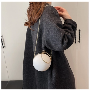 Detail of white spherical acrylic evening bag with gold ring handle on a tweed jacket
