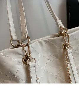 Close-up of golden metal hook hardware on white quilted faux leather tote bag