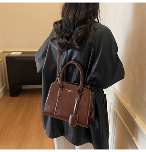 Detail of red-brown glossy leather handbag with gold logo shown on model's shoulder