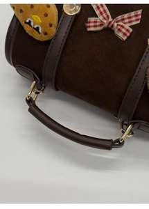Close-up of brown suede handbag with leather handle, plaid bow, and plush cookie charm