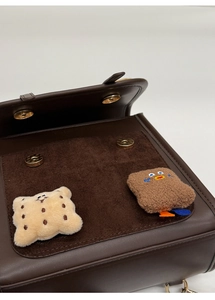 Detail of dark brown leather bag flap with two magnetic buckles and cartoon embroidery