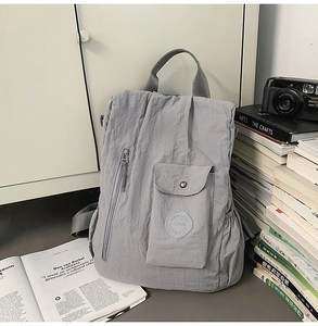Detail of light grey nylon backpack with side flap pocket and round brand logo patch