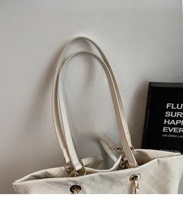 Detail of white quilted tote bag with gold chain strap and leather handle texture