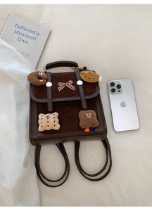 Flat lay of small brown backpack with cute cartoon plush patches and red bow detail