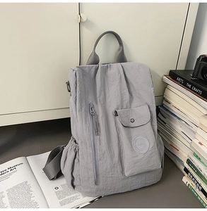Detail of grey crinkled nylon backpack showing vertical zipper pocket and logo