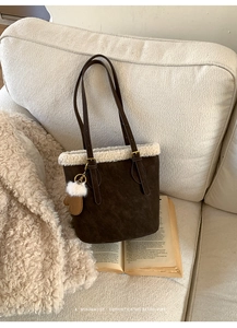 Detail of dark brown suede bucket bag with faux fur trim and plush heart charm on a sofa
