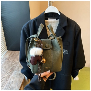 Detail of dark green bucket bag with white contrast stitching and decorative charms