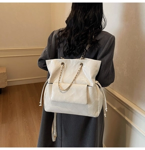 Detail of white quilted tote bag featuring glossy finish and elegant metal chain pocket