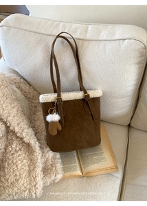 Detail of a brown suede bucket bag with white faux fur trim and a heart pendant