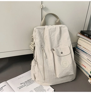 Detail of cream pleated nylon backpack showing front zip pocket and textured fabric