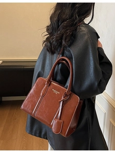 Vintage brown leather handbag with top handles and shoulder strap worn by a fashion model