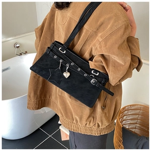 Detail of black suede shoulder bag with silver eyelets, star patch, and heart charm
