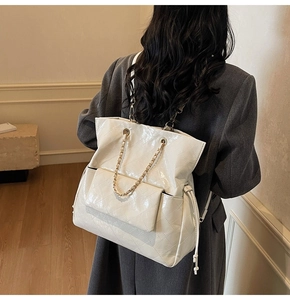 Detail of white quilted patent leather backpack featuring metal chain and adjustable drawstring
