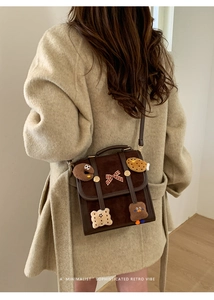 Detail of retro dark brown suede bag with cute biscuit charms on a beige coat background