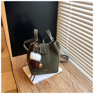 Detailed view of green suede bucket bag with white stitching and plush charm