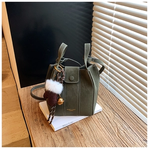 Detail of dark green suede bucket bag with white stitching and brown plush glove charm