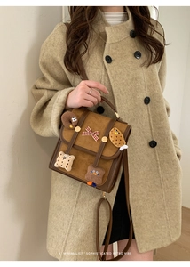 Close-up of retro brown messenger bag featuring cute plush patches and a checkered bow