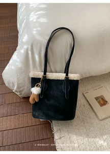 Détail d'un sac cabas en daim noir avec bordure en laine blanche et breloque gant marron