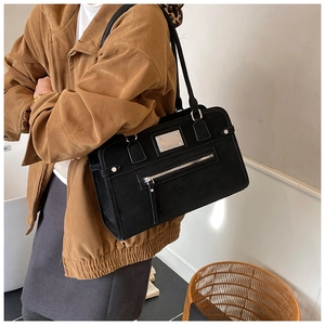 Detail of black matte shoulder bag with silver metal plaque and exterior zipper pocket
