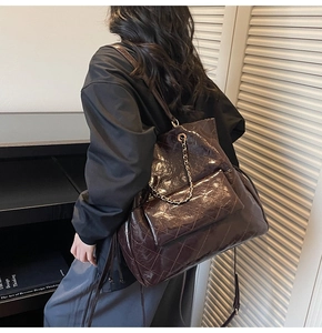 Detail of dark brown quilted tote bag with metal chain on oil-waxed leather surface