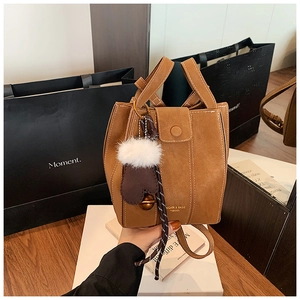 Detailed view of brown suede bucket bag with white stitching and plush ball charm decoration