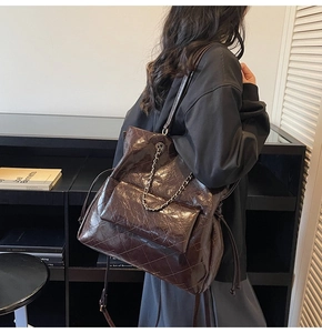 Detail of dark brown tote bag with glossy diamond texture and metal chain in daily use
