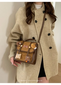 Detail of vintage brown suede crossbody bag with plush charms on a neutral coat model