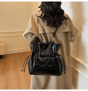 Detail of black glossy tote bag featuring quilted textures and decorative metal chain