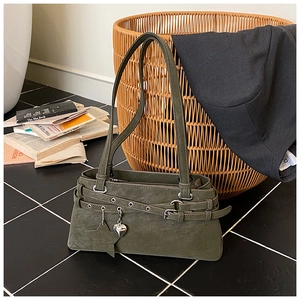 Detail view of dark olive green suede shoulder bag with heart pendant on tiled floor