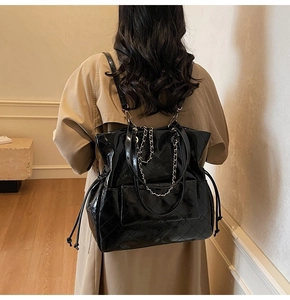 Detail of a shiny black quilted tote bag with chain strap shown on a model