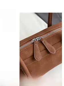 Detail of silver dual zippers and contrast stitching on a brown pebbled leather bag