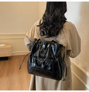 Rear view of model wearing a black quilted leather tote bag with chain and drawstring