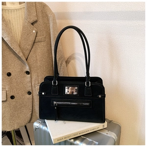 Detail of a matte black leather handbag on a silver suitcase with business attire