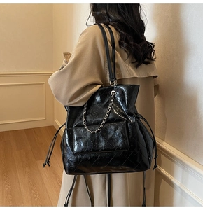 Quilted black leather tote bag with silver chain detail shown on shoulder of a model