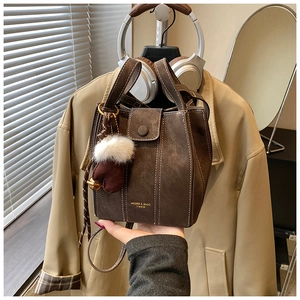 Detail view of brown bucket bag with white stitching and plush glove charm accent