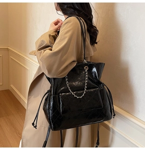 Detail of black glossy quilted tote bag with metal chain and side drawstring on model