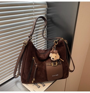 Detail of dark brown suede tote bag with front buckle pocket and plush bear pendant
