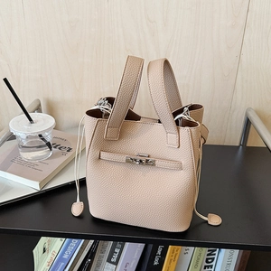 Detail of beige lychee grain leather bucket bag featuring a silver twist lock and dual handles
