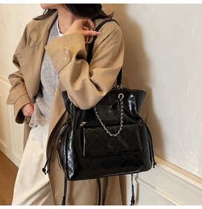Detail of black quilted tote bag featuring silver chain straps and side drawstring