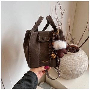 Detailed macro shot of dark brown suede bucket bag with contrast stitching and charms