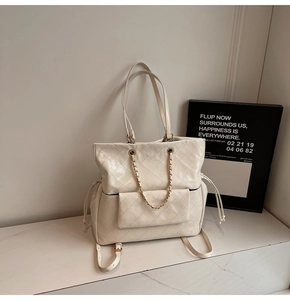 Detailed close-up of quilted cream tote bag featuring gold chain and side drawstring