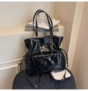 Detail of black quilted tote bag with shiny finish, silver chain, and drawstring side details