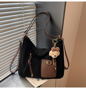 Detail of black suede hobo bag with brown pocket, gold buckle and cute bear charm