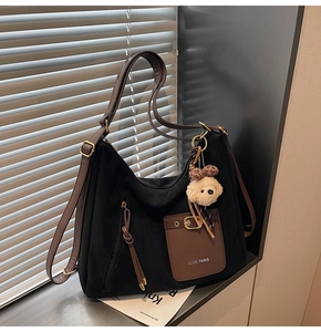 Close-up of black canvas tote with brown leather pocket and a cute teddy bear charm