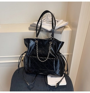 Detail of black glossy quilted tote bag featuring metallic chain and drawstring closure